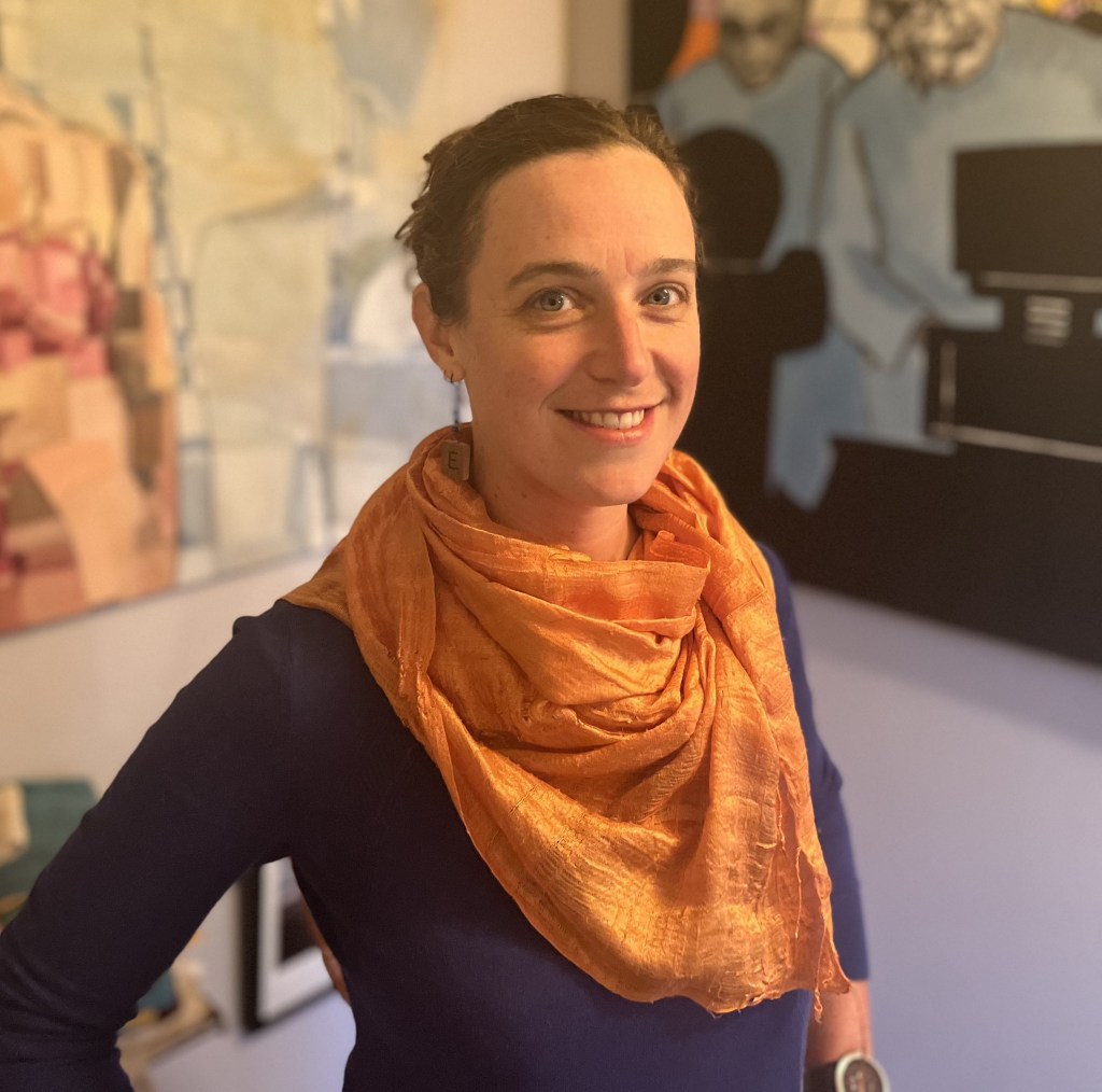 Elisabeth Reinkordt wearing a bright orange shawl, standing in front of abstract paintings